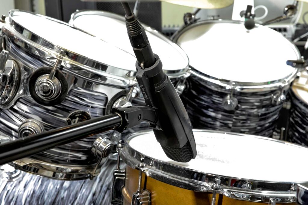 A Sennheiser MD421 with a black MicLock clip arm over a drum set.